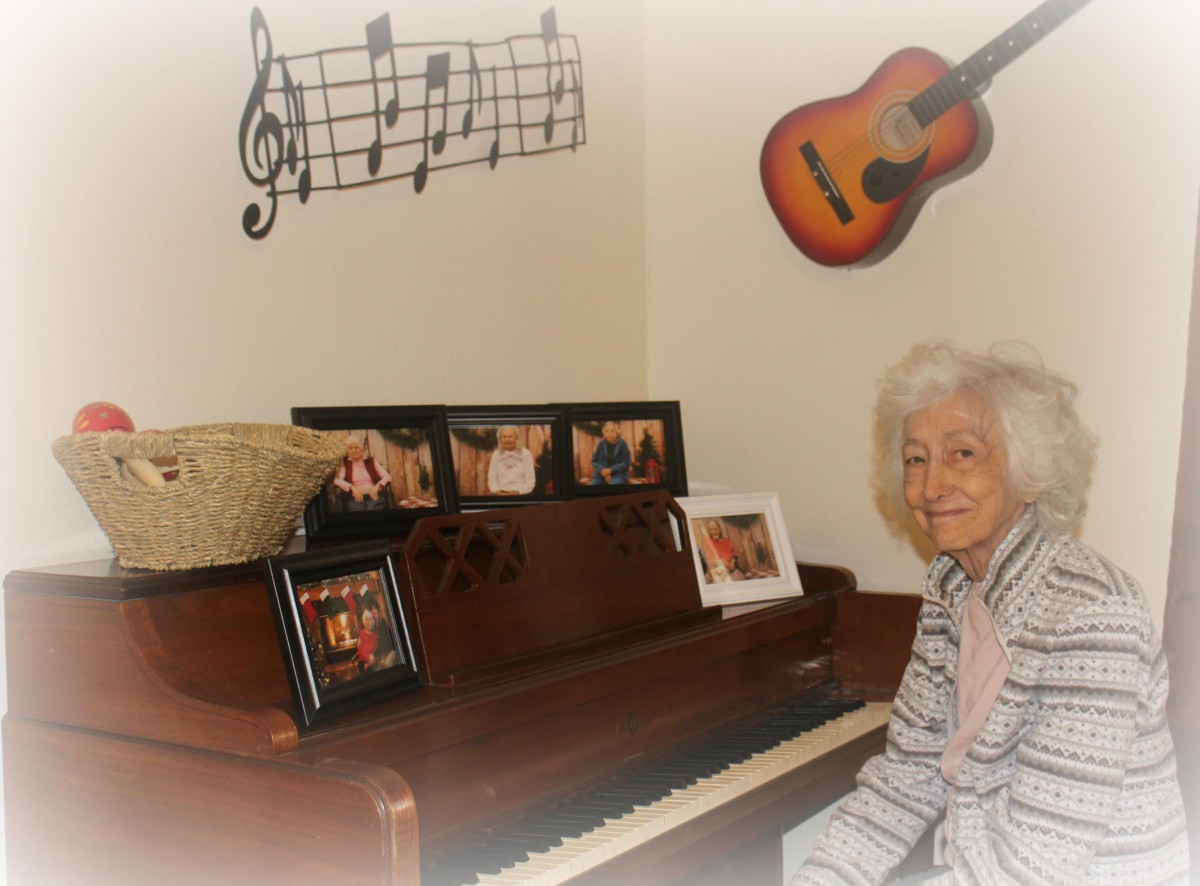 An elderly person sits by a piano in a room decorated with music notes and a guitar on the wall.