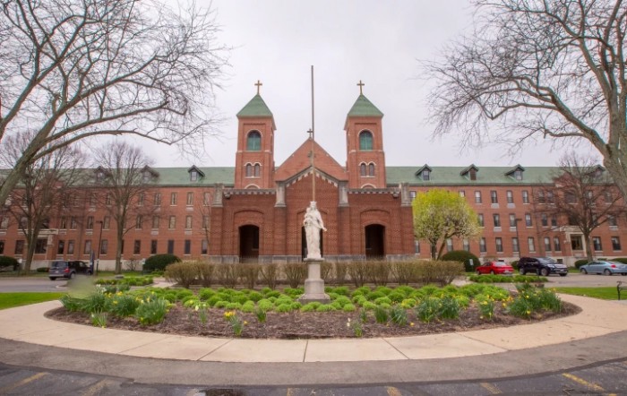 A brick church with twin towers and a statue in the foreground, surrounded by landscaped gardens.