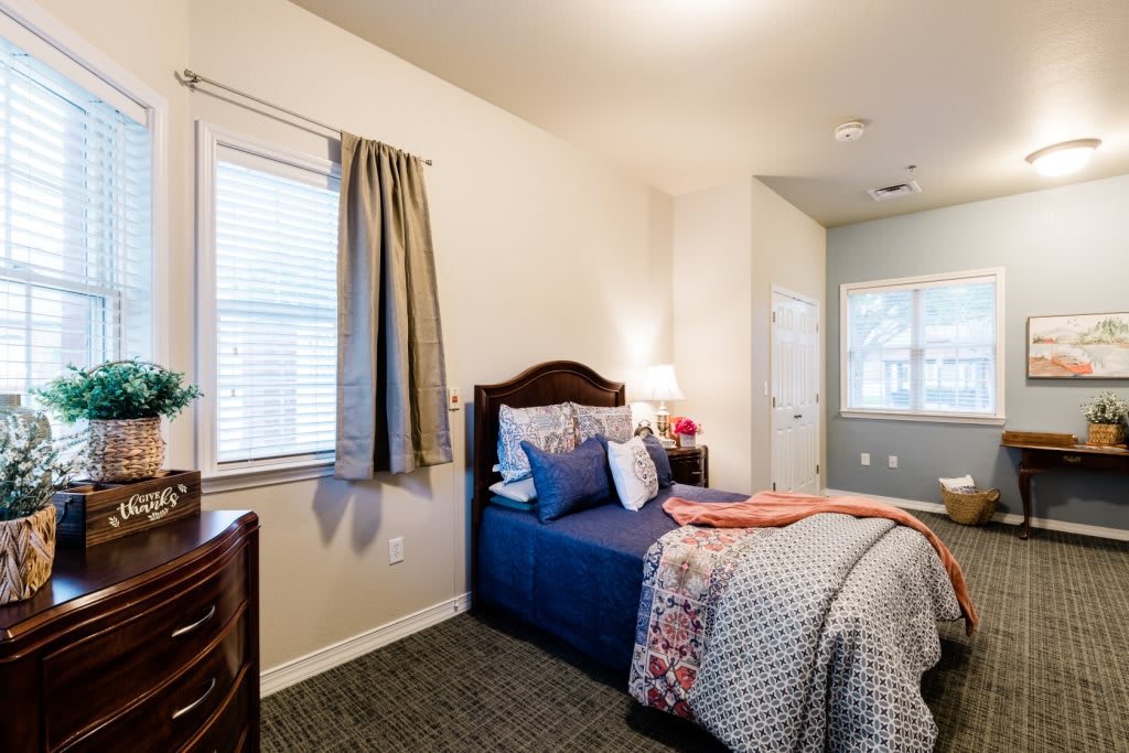 A cozy bedroom with a single bed, decorated with patterned bedding and pillows, next to a window with curtains.