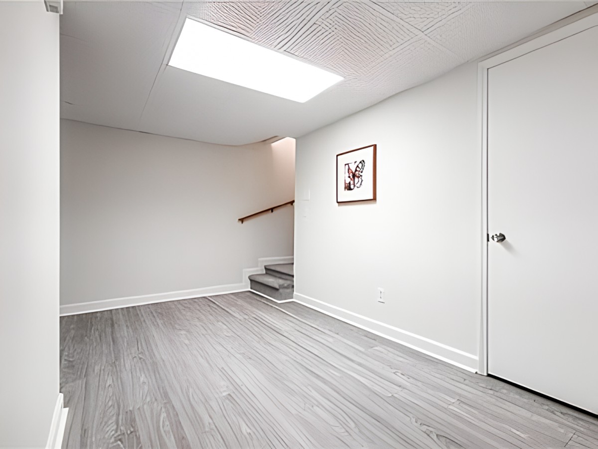 A minimalist room with a skylight, wooden flooring, and a small staircase.