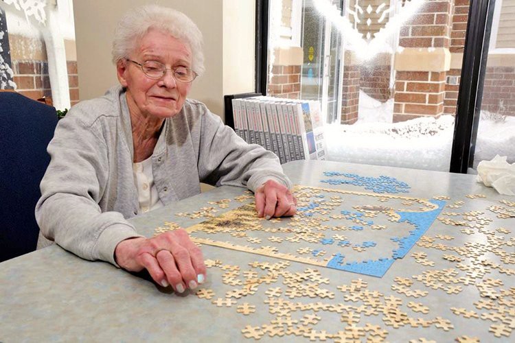 A senior woman working on a puzzle at a table during the day.