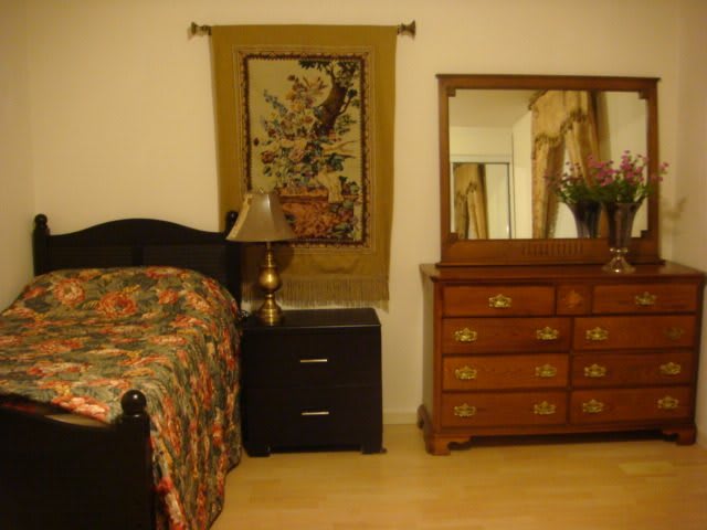 A cozy bedroom featuring a wooden bed with floral bedding, a matching dresser with mirror, and a decorative tapestry on the wall.
