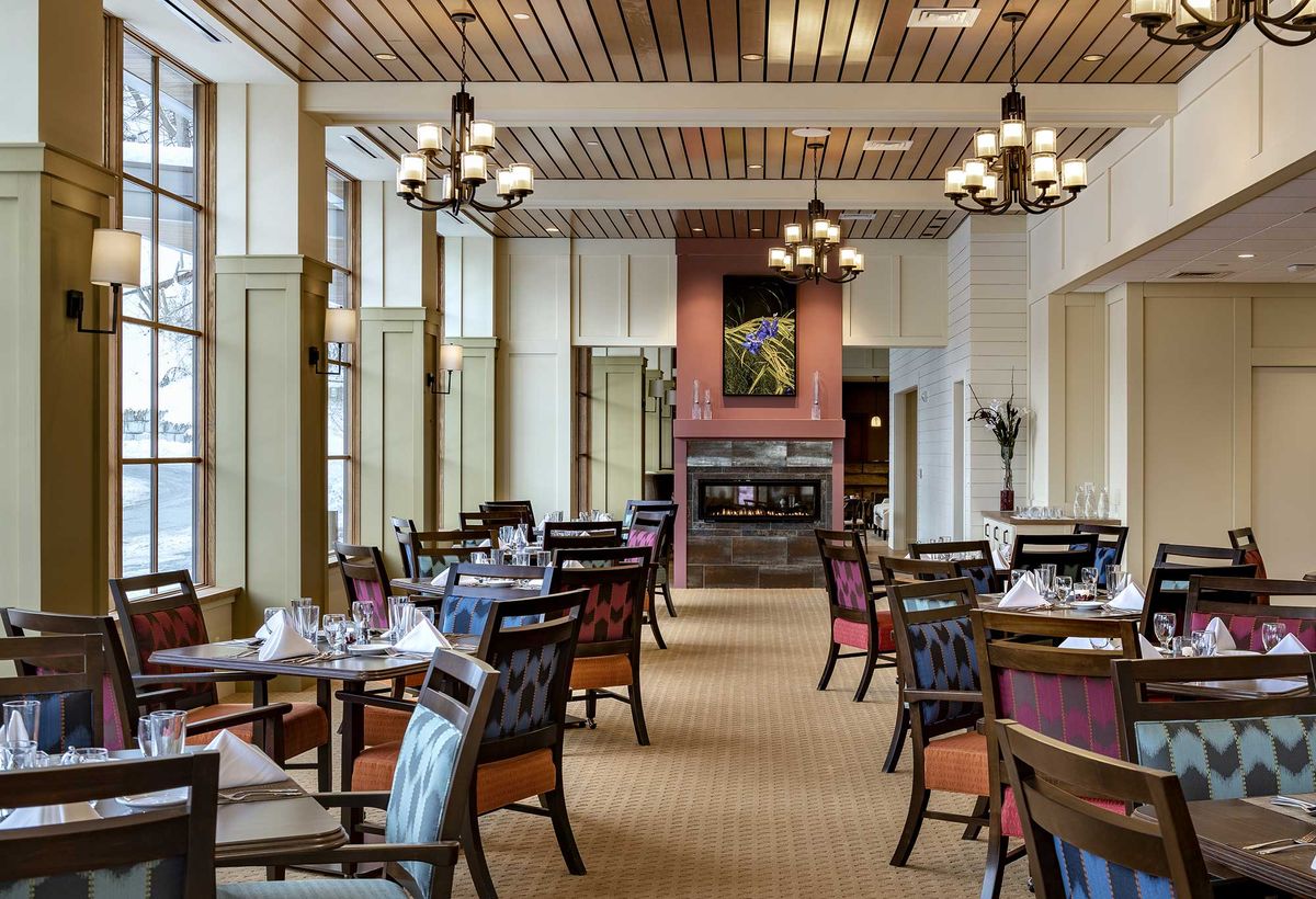 An elegant dining area with beautifully set tables, chandeliers, and a cozy fireplace.