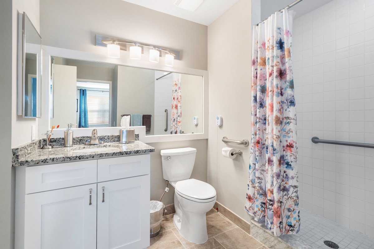 A modern bathroom featuring a floral shower curtain, white cabinetry, and vanity lights.