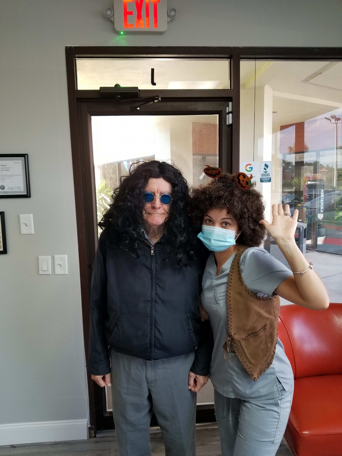 Two people dressed in playful costumes, one wearing a mask and waving.