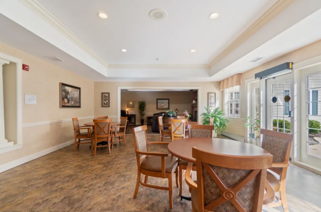 A spacious dining area with wooden tables and chairs, illuminated by natural light.