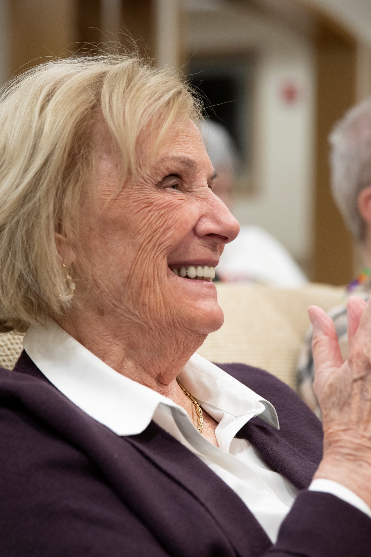 An elderly woman smiling and clapping indoors.