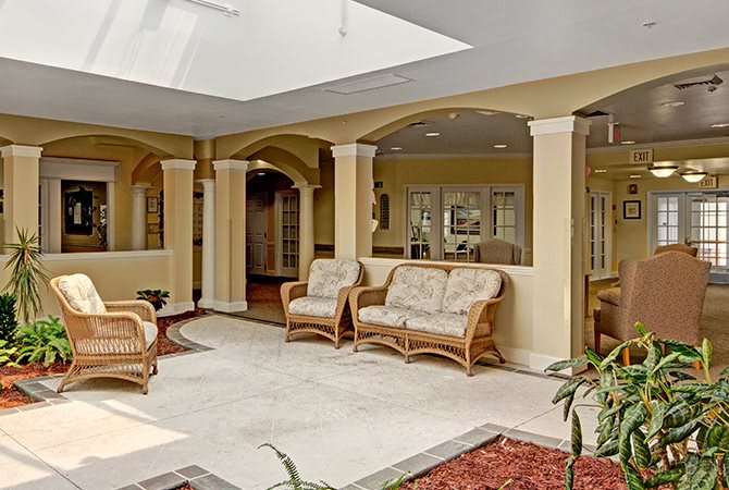 A spacious lobby area with wicker furniture and a skylight, surrounded by columns and decorative indoor plants.
