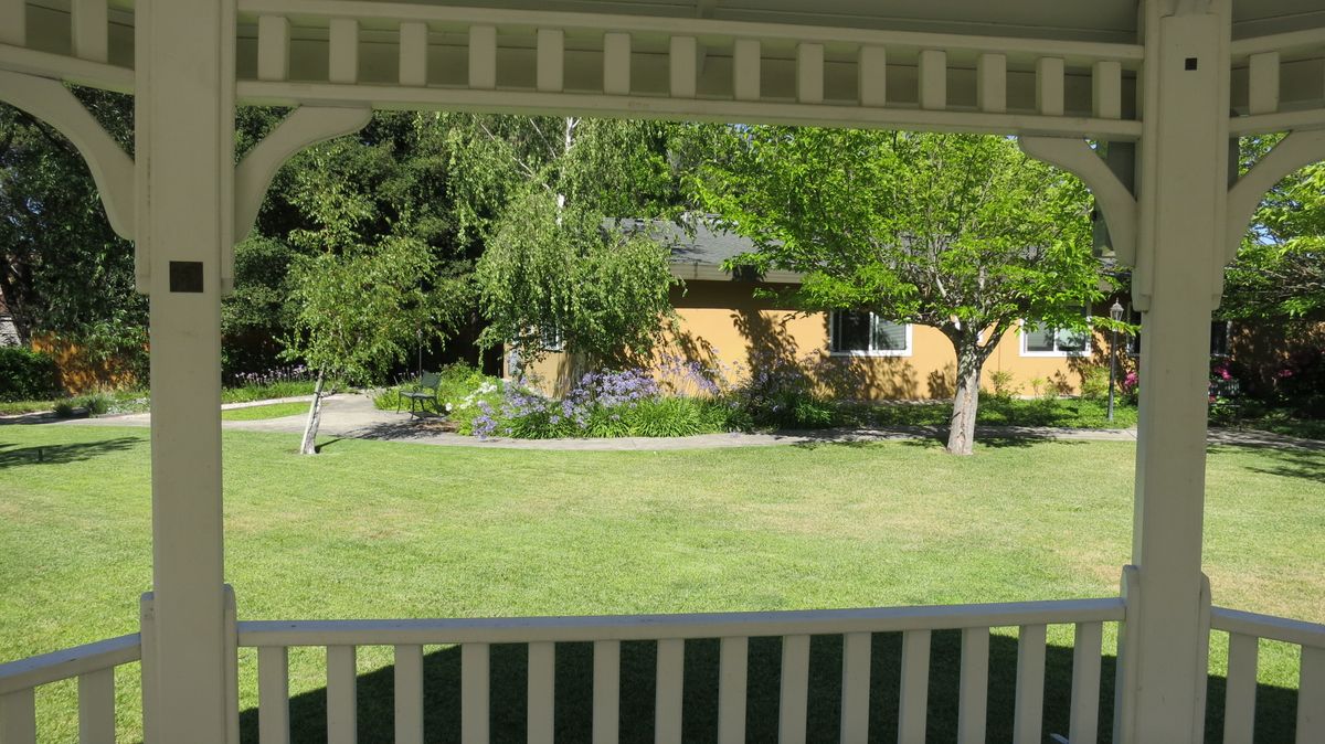 A view of a house and garden with trees and a well-maintained lawn, seen from a porch.
