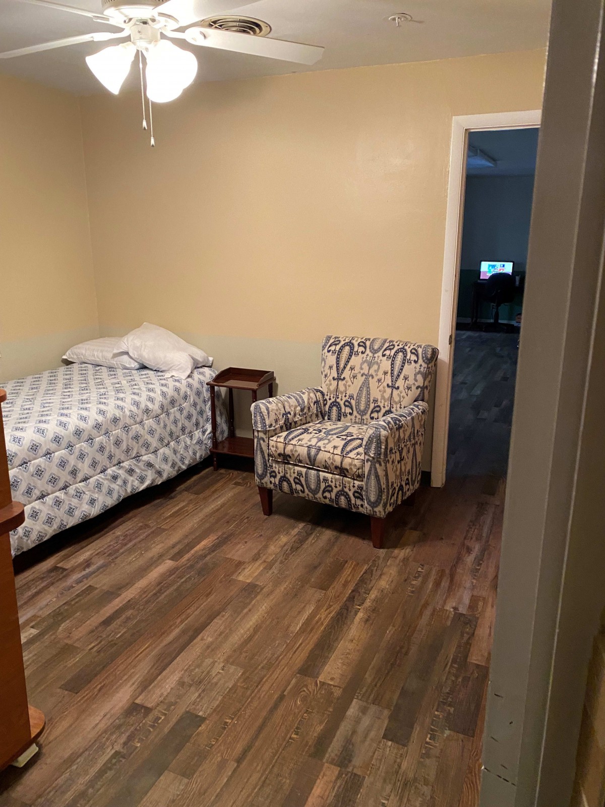 A simple bedroom with a single bed and patterned armchair.