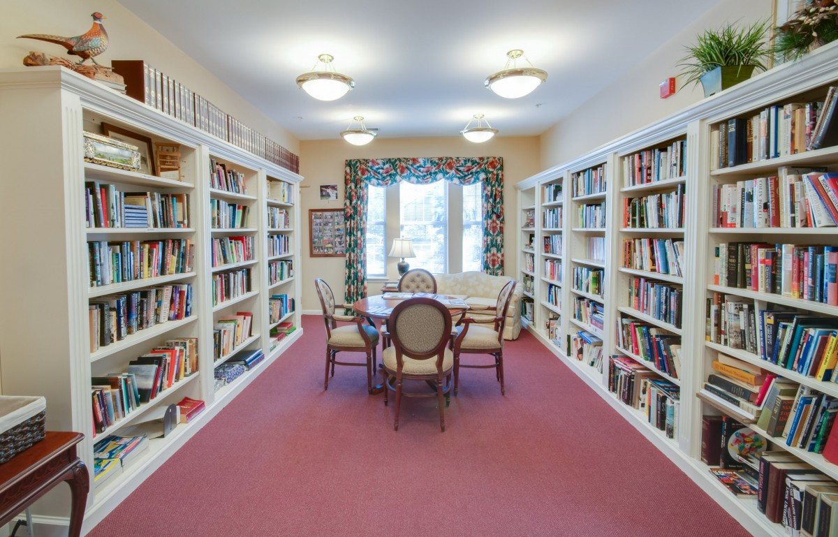A cozy library room with bookshelves lining the walls, centered by a table and chairs.