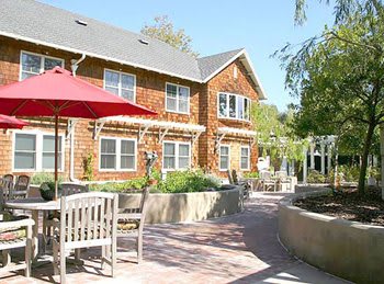 A view of a sunny patio area with outdoor seating and a brick path in front of a residential building.