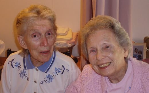 Two elderly women smiling indoors.