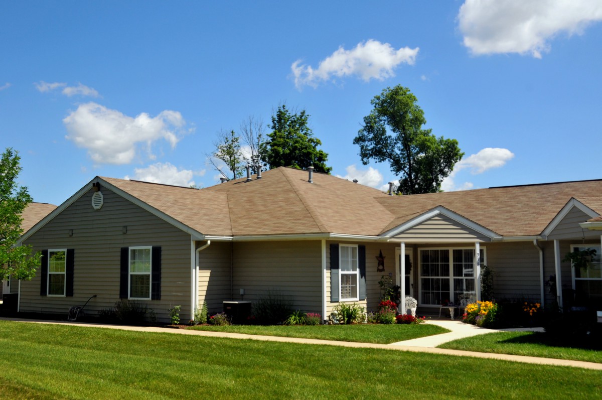 A single-story suburban house with a well-maintained lawn under a blue sky with clouds.
