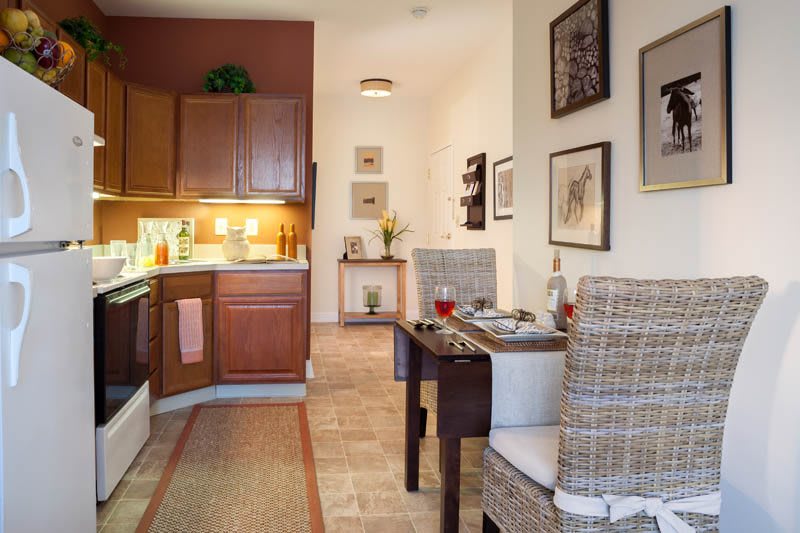 A cozy kitchen and dining area with wooden cabinets, rattan chairs, and decorative wall art.