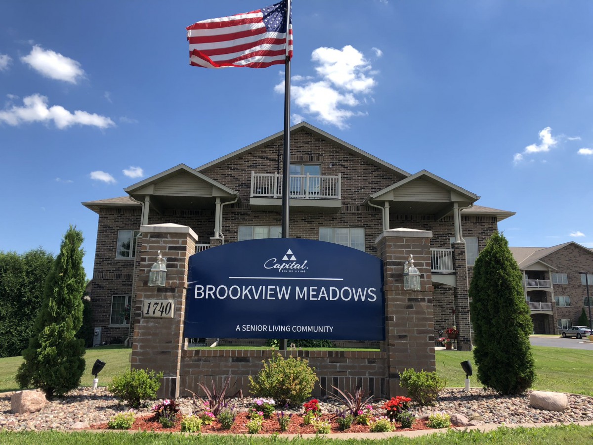 Brookview Meadows apartment building with an American flag and garden in front.