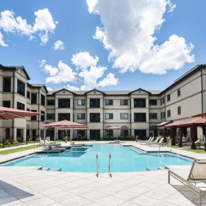 A sunny day at a modern apartment complex featuring an inviting outdoor pool and seating areas.