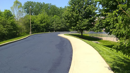 A winding road accompanied by a smooth sidewalk and lush greenery.