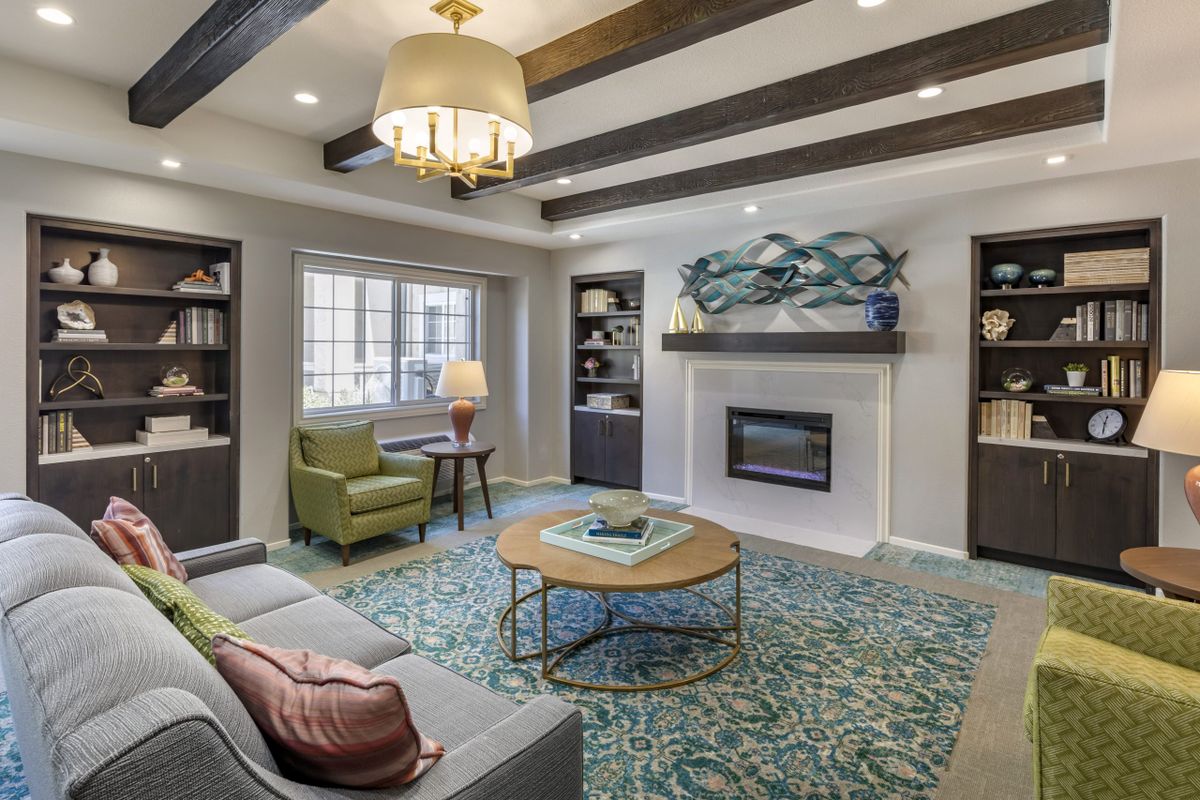 A stylish living room featuring a sofa, armchair, and fireplace with decorative ceiling beams and bookshelves.
