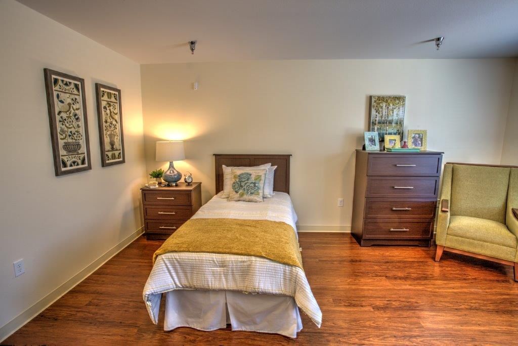 A cozy bedroom with a single bed, wooden floor, and warm lighting.