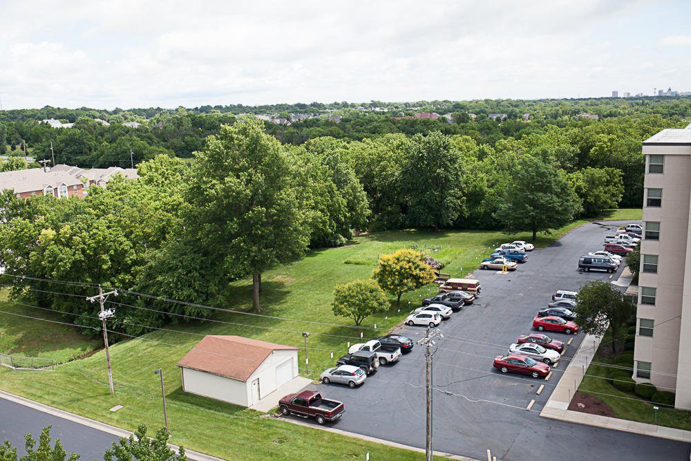 Aerial view of a parking lot adjacent to a green, tree-filled landscape.