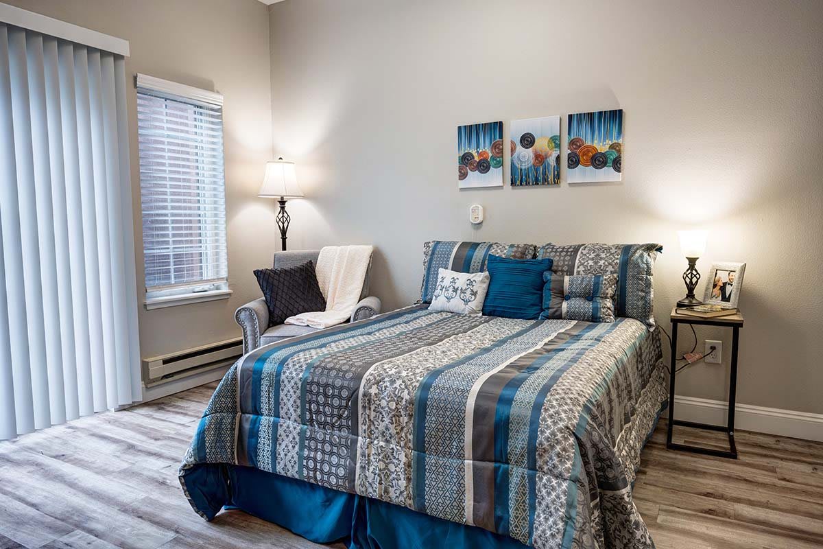A cozy bedroom with a patterned comforter, artwork above the bed, and a window providing natural light.