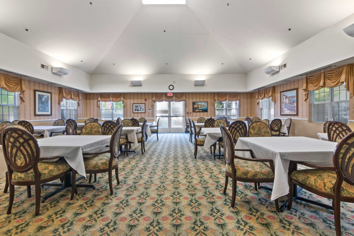 A well-lit dining room with multiple tables and chairs arranged neatly on a patterned carpet.