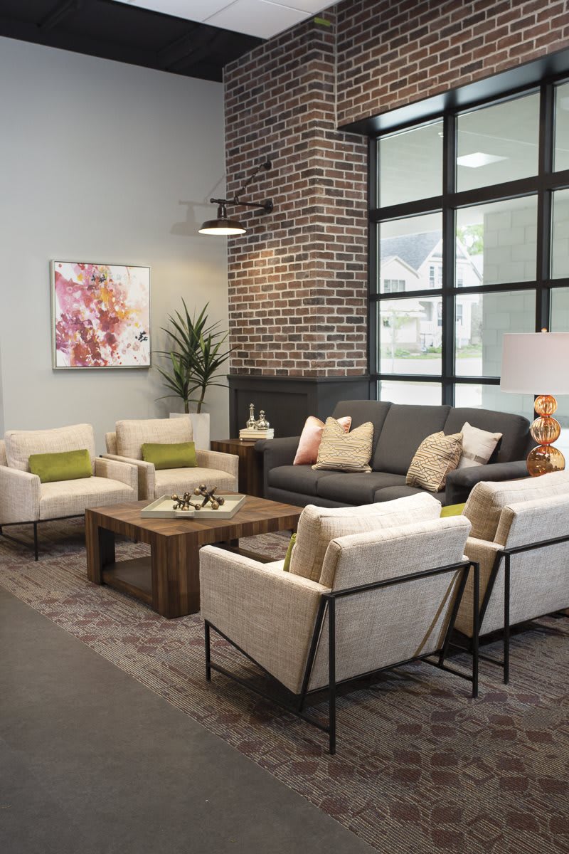 A modern living room with a gray sofa, cream chairs, and a wooden coffee table, complemented by a brick accent wall and decorative plants.