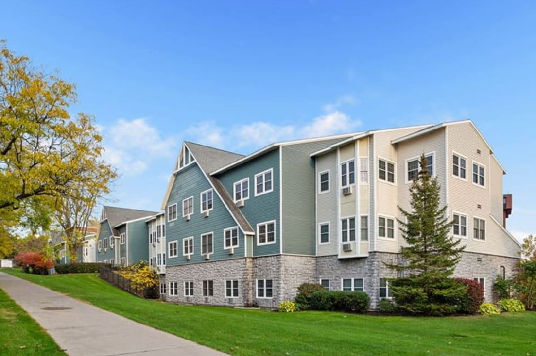 A modern residential apartment building with a scenic landscape and a clear blue sky.