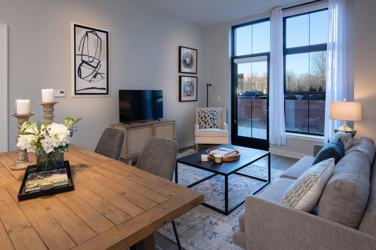 A modern living room with a dining area, featuring stylish decor and large windows.