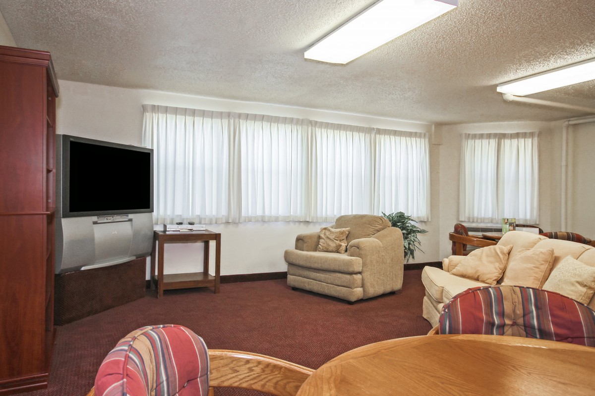A cozy living room with armchairs, a television, and large windows with blinds.