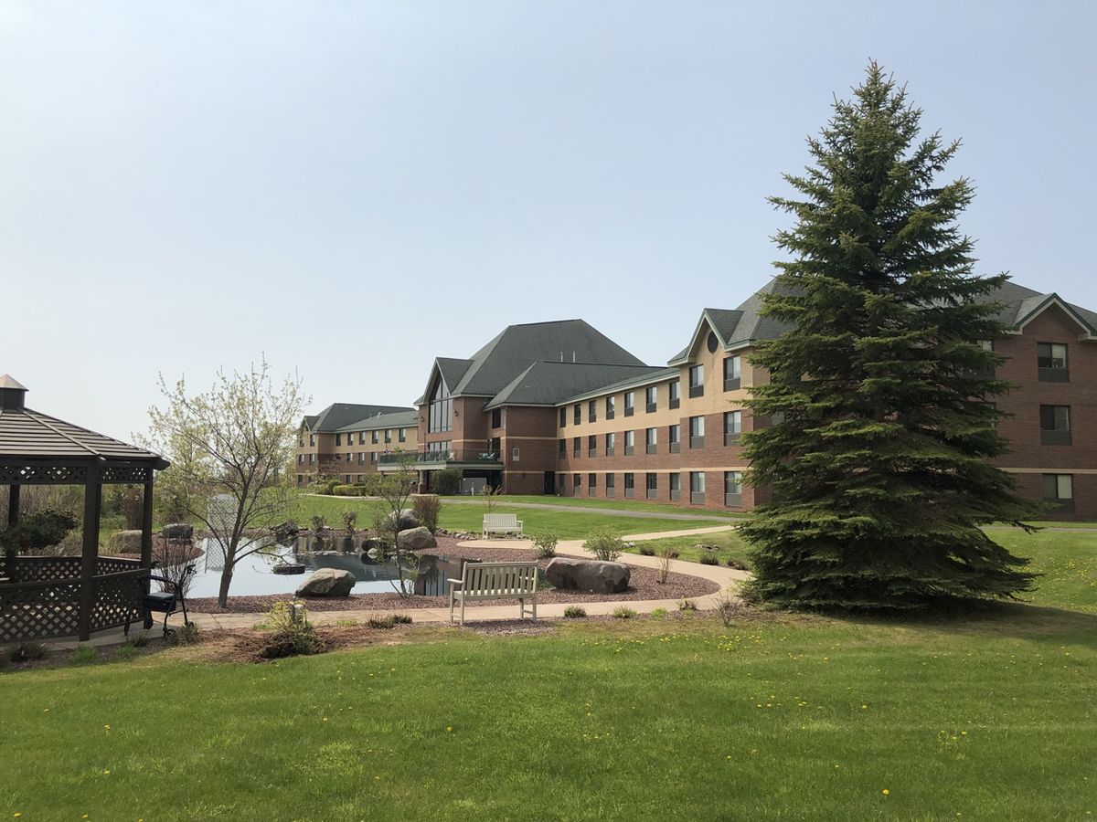 A large brick building with a well-maintained garden and trees in the foreground.