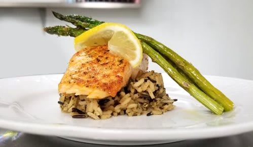 A plate featuring a grilled chicken breast on a bed of rice, garnished with asparagus and a lemon slice.