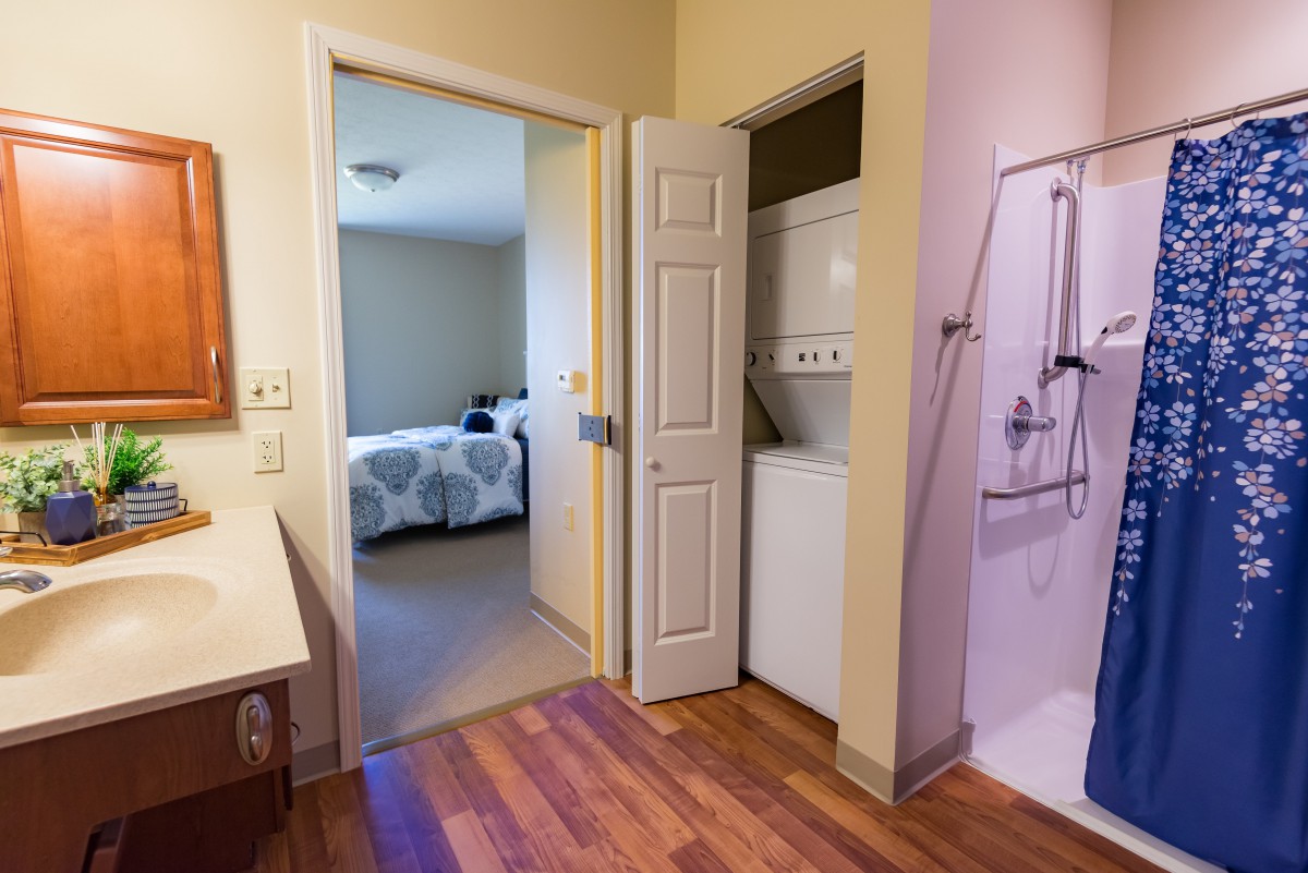 A view of a bathroom with an adjacent laundry area leading into a bedroom.