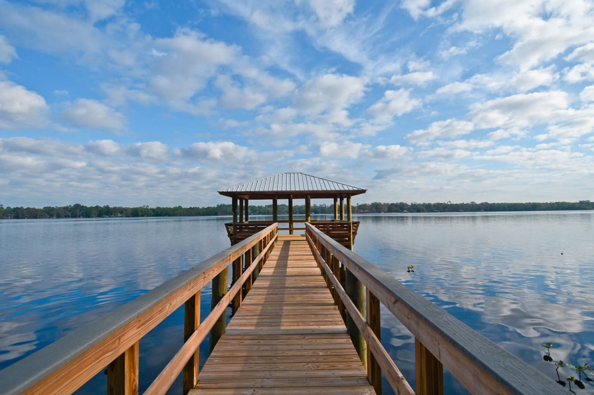A serene view of a wooden dock extending over a calm lake under a partly cloudy sky.
