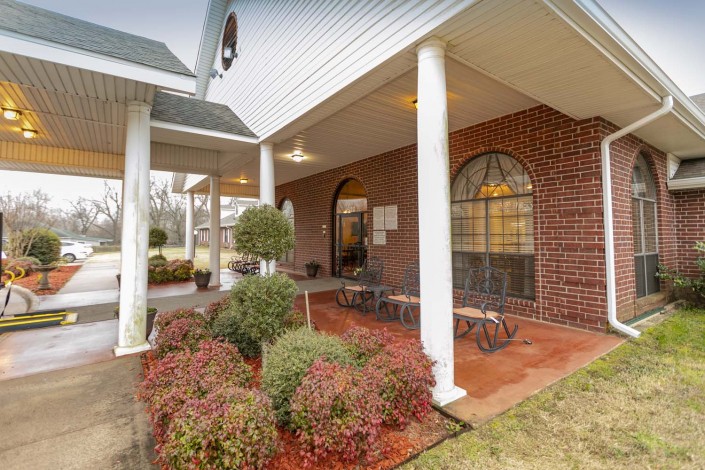 A welcoming building entrance with a covered porch, white columns, and landscaped greenery.
