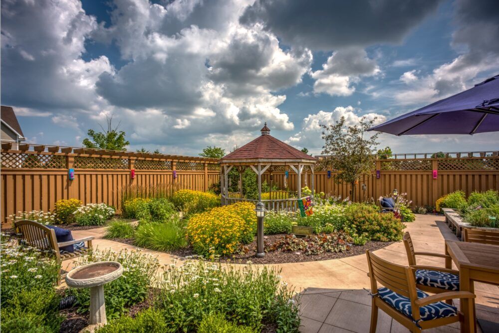 A beautifully landscaped garden featuring a central gazebo surrounded by vibrant flowers and greenery, under a partly cloudy sky.