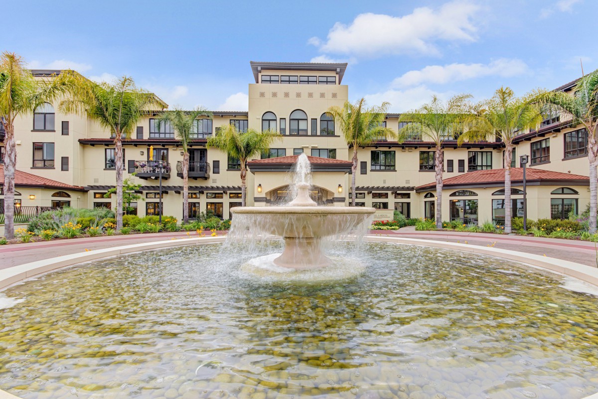 A luxurious building with a large fountain in the foreground, surrounded by palm trees on a sunny day.