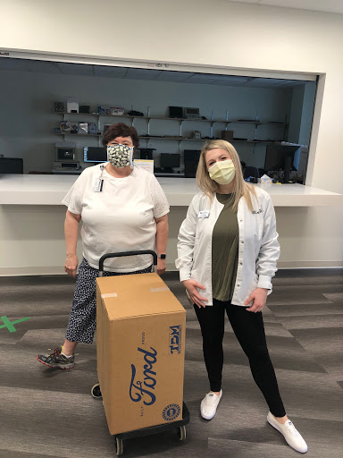Two women wearing masks in an indoor environment next to a boxed item.