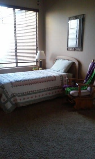A cozy bedroom with a single bed, patterned quilt, and a rocking chair by the window.