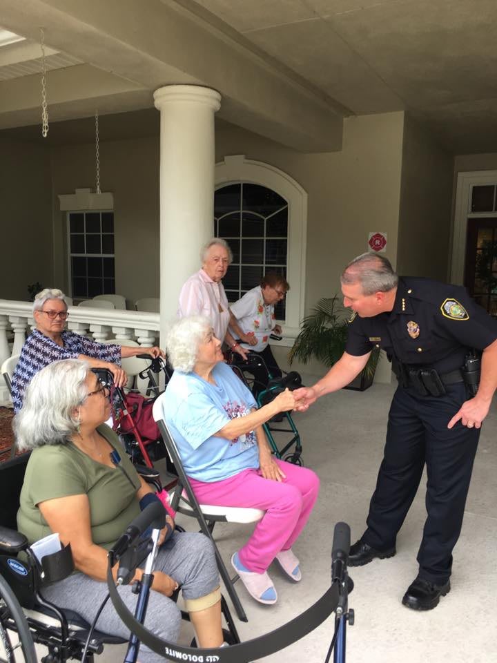 A police officer interacts with elderly residents, shaking hands and fostering community relations.