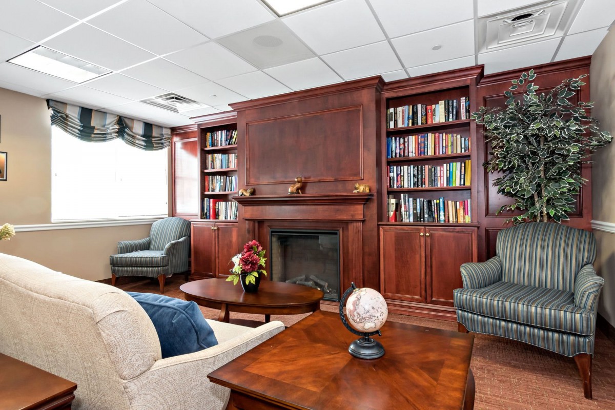 A cozy library room with bookshelves, a fireplace, and comfortable seating arrangements.