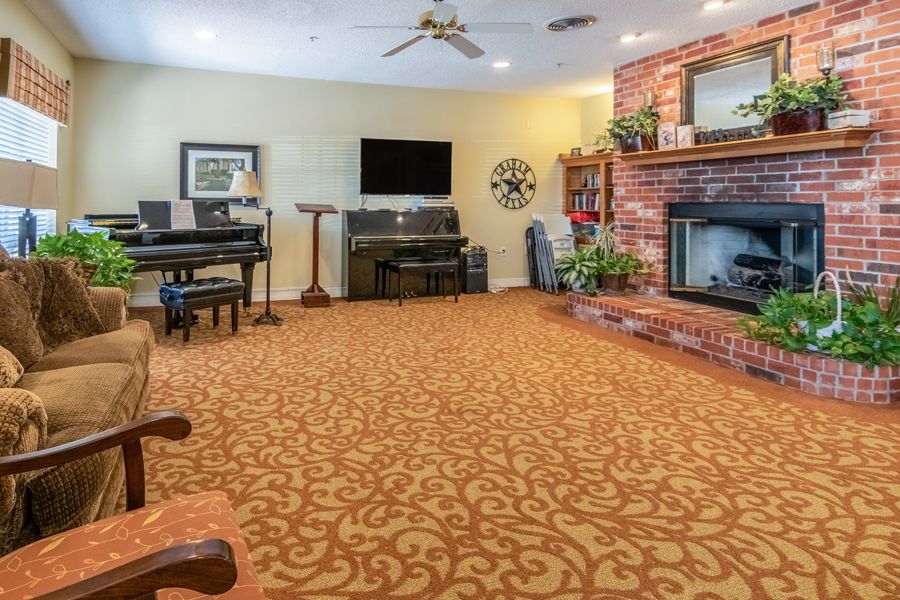 A cozy living room with a piano, brick fireplace, and ornate carpet.
