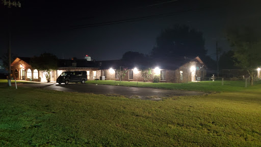 A well-lit house at night with a parked vehicle and lush green grass.