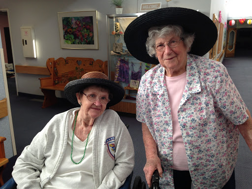 Two elderly women wearing stylish hats, enjoying each other's company indoors.