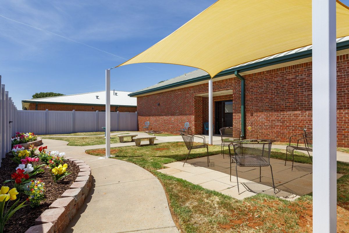 A sunny courtyard featuring a shade sail, patio furniture, and landscaped surroundings.