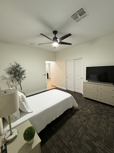 A serene and modern bedroom featuring minimalistic decor, a ceiling fan, and a television.