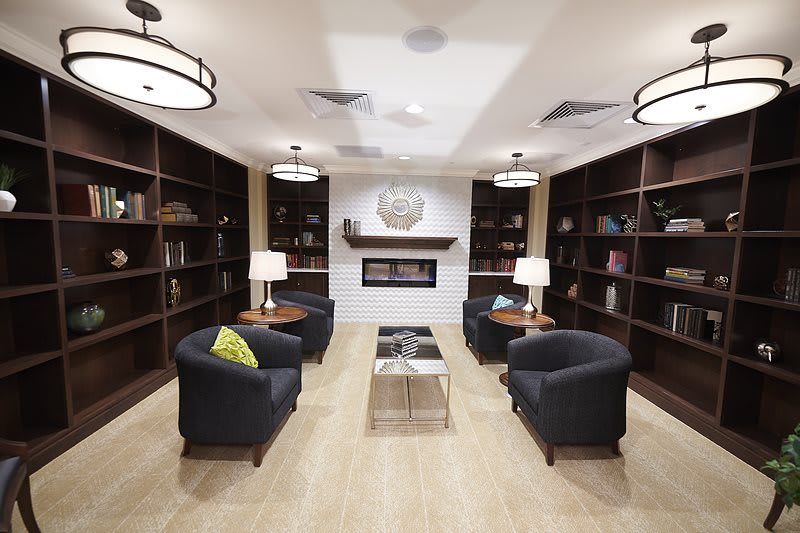 A modern library seating area with armchairs, bookshelves, and a central fireplace.