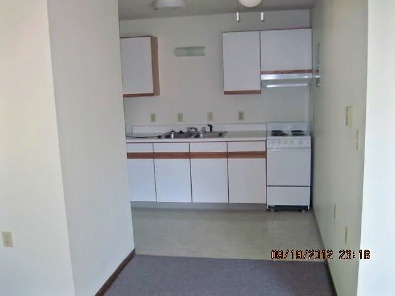 A small apartment kitchen with white cabinets, a stove, and a sink.