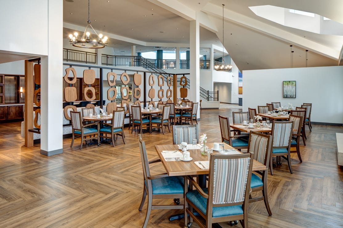 A spacious and elegantly designed restaurant interior featuring neatly arranged tables and chairs, with decorative elements and chandeliers.